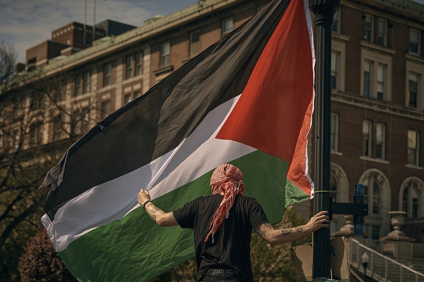A protester places a Palestinian flag at a pro-Palestinian encampment at Columbia University, in New York, Sunday, April 28, 2024, advocating for financial disclosure and divestment from all companies ...