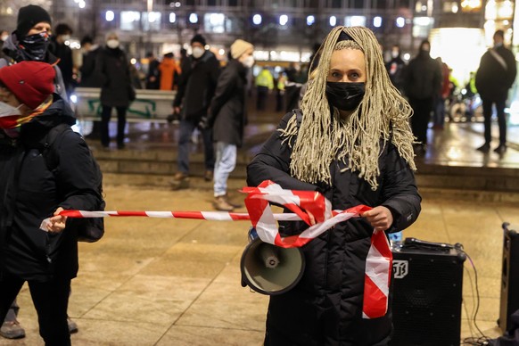 Irena Rudolph-Kokot (l, SPD), hält bei einer Demonstration gegen die Anti-Corona-Proteste ein rot-weisses Absperrband am Denkmal &quot;Demokratieglocke&quot; auf dem Augustusplatz. In der Leipziger In ...