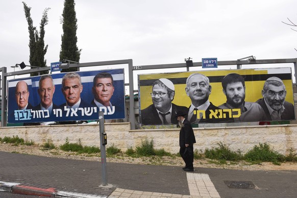 A man walks past an election billboards, put up by the new Israeli centrist Blue and White party, featuring Israeli Prime Minister Benjamin Netanyahu (second from the left in right billboard) with ext ...