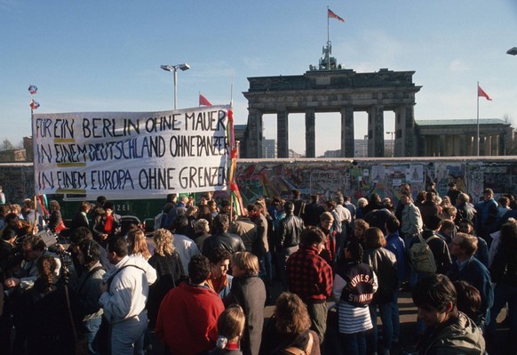 Menschen protestieren vor der Berliner Mauer fuer die Wiedervereinigung. Im Hintergrund das Brandenburger Tor. Berlin, 09.11.1989, Berlin Deutschland PUBLICATIONxINxGERxSUIxAUTxONLY Copyright: xThomas ...