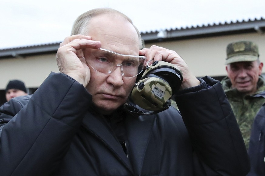 Russian President Vladimir Putin attaches a protective glasses as he visits a military training centre of the Western Military District for mobilised reservists in Ryazan Region, Russia, Thursday, Oct ...