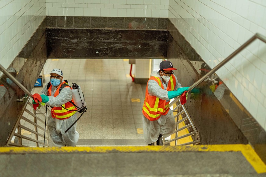 Zwei Personen desinfizieren in einer New Yorker U-Bahn-Station das Geländer.