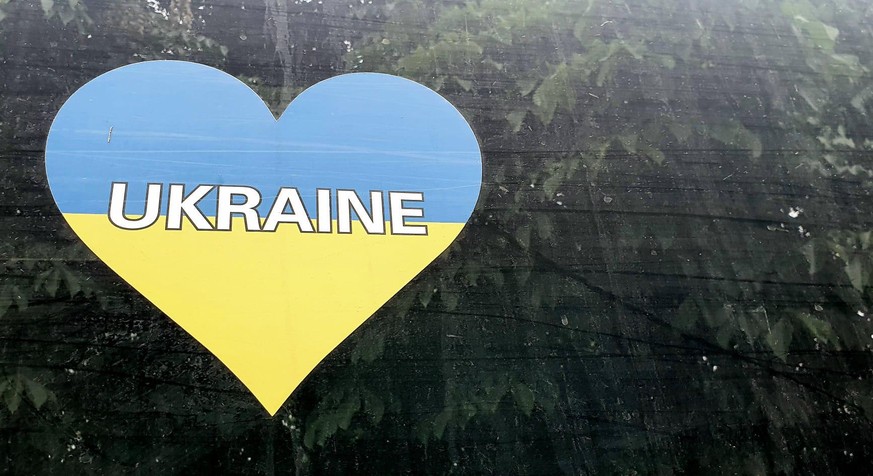 Ein Herz in den Farben der Ukrainischen Flagge mit der Aufschrift &quot;Ukraine&quot; auf dem Fenster eines Evakuierungsfahrzeugs