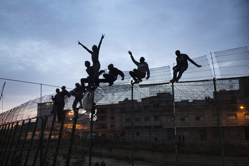 FILE - Sub-Saharan migrants climb over a metallic fence that divides Morocco and the Spanish enclave of Melilla on Friday, March 29, 2014. Since the early 1990s, Spain has built six-meter (20-foot) la ...