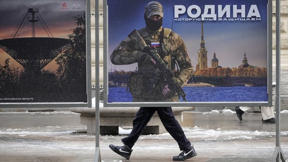 ARCHIV - 20.02.2023, Russland, St. Petersburg: Ein Mann geht an einem Plakat mit dem Bild eines russischen Soldaten und der Aufschrift «Wir verteidigen das Vaterland» vorbei, während einer Straßenauss ...