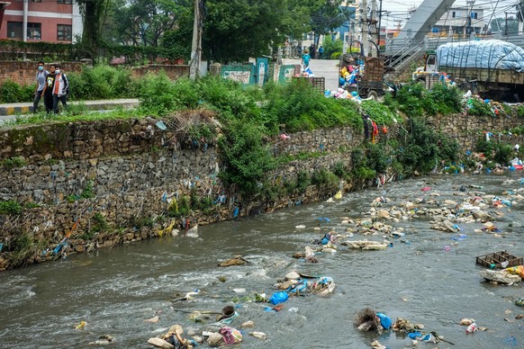 KATHMANDU,NEPAL-JUNE 4: Garbage bags are seen floating on the river as people walk beside the river in Kathmandu, Nepal on June 4, 2022. Rivers in Nepal are polluted by different chemicals and effluen ...