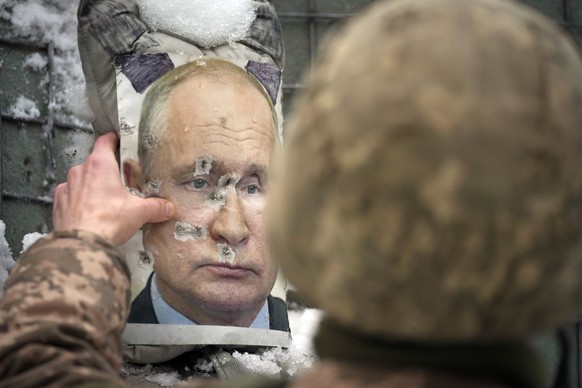 ARCHIV - 01.02.2022, Ukraine, Luhansk: Ein ukrainischer Soldat justiert ein von Kugeln durchl�chertes Bild des russischen Pr�sidenten Putin w�hrend eines Interviews mit Medienvertretern an einer Front ...