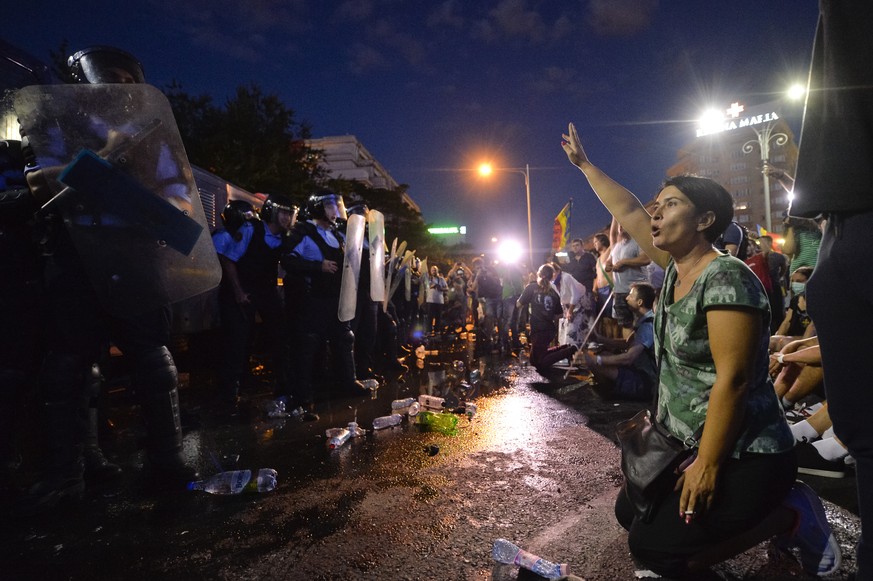 A woman shouts slogans in front of a riot police line during protests outside the government headquarters, in Bucharest, Romania, Friday, Aug. 10, 2018. Romanians who live abroad are staging an anti-g ...