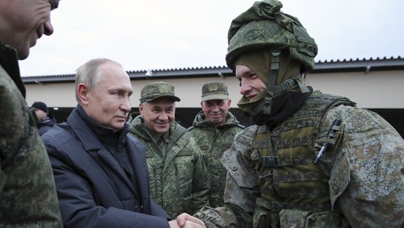 ARCHIV - 20.10.2022, Russland, Rjasan: Der russische Präsident Wladimir Putin schüttelt einem Soldaten die Hand, und der russische Verteidigungsminister Sergej Schoigu steht lächelnd neben ihm, währen ...