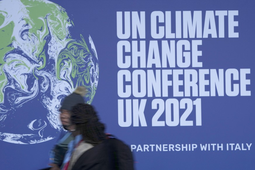 FILE - In this Oct. 29, 2021 file photo attendees walk past a banner at the venue where COP climate conference will be held in Glasgow, Scotland. The U.N. climate summit, known as COP26 this year, bri ...