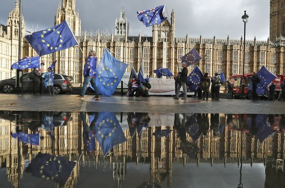 FILE - Protestors are reflected in a large puddle as they wave European flags to demonstrate against Brexit in front of the Parliament in London, Dec. 3, 2018. The U.K. election in December 2019 was b ...