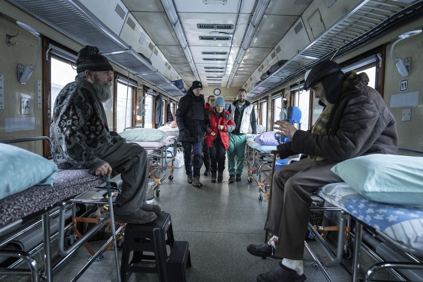 14.02.2023, Ukraine, Pokrowsk: Rettungssanitäter helfen einer älteren Frau, ihren Sitzplatz im medizinischen Zug von Ärzte ohne Grenzen einzunehmen, der Patienten aus der Nähe der Frontlinien der Kämp ...