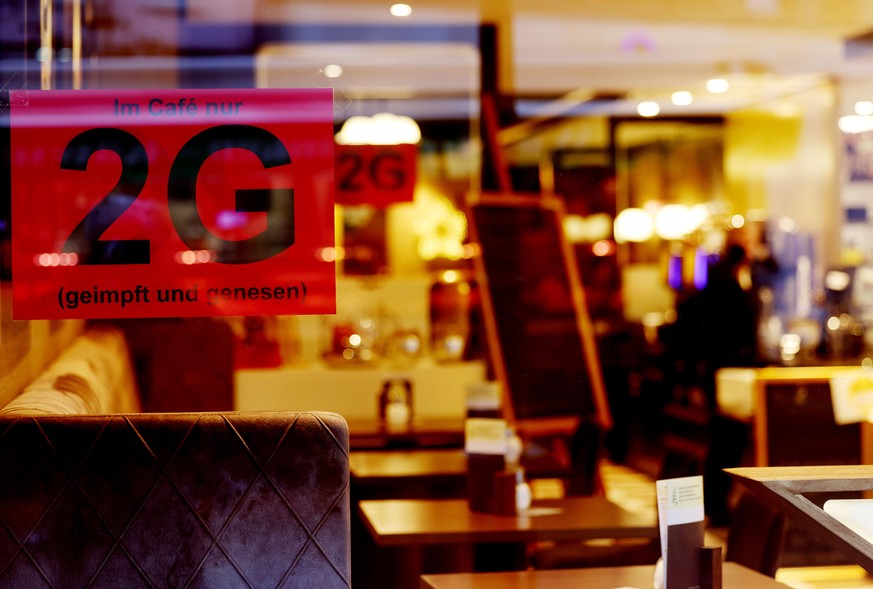 Ein Schild, das auf die 2G Regeln hinweist, hängt in einem Cafe. In Nordrhein-Westfalen gelten strengere coronabedingte Einschränkungen. Im Freizeitbereich gelten flächendeckend Zugangsbeschränkungen  ...