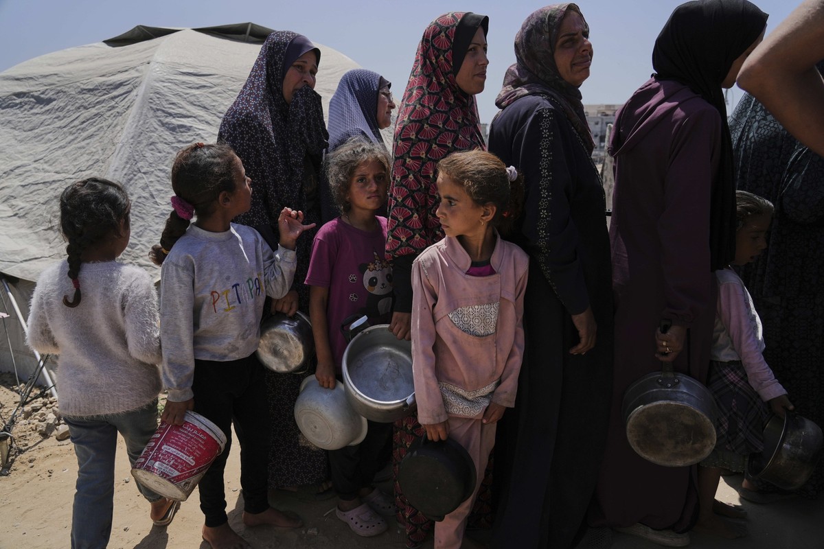 21.05.2025, Palästinensische Gebiete, Gaza-Stadt: Vertriebene Palästinenser stellen sich in einem Zeltlager in Gaza-Stadt auf, um gespendete Mahlzeiten aus einer Gemeinschaftsküche zu erhalten. Foto:  ...