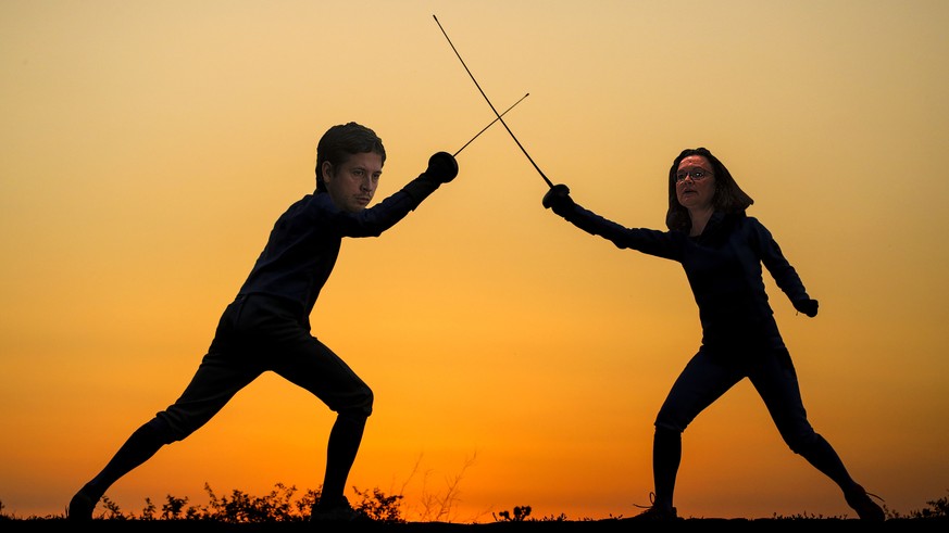 Silhouette of a young man and woman fencing.