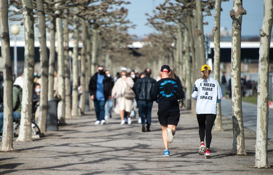 ARCHIV - 20.02.2021, Nordrhein-Westfalen, Düsseldorf: Ein Frau, die ein Shirt mit der Aufschrift «I need time and space» trägt und ihr Begleiter joggen an der Rheinuferpromenade entlang. (Zu dpa: «Meh ...