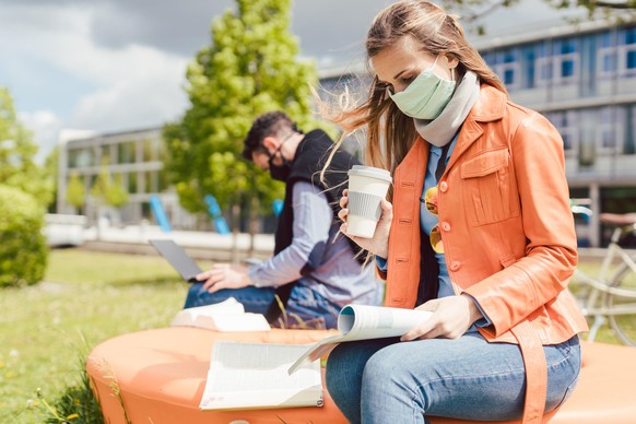 Woman student on college campus learning wearing face mask while working on her laptop