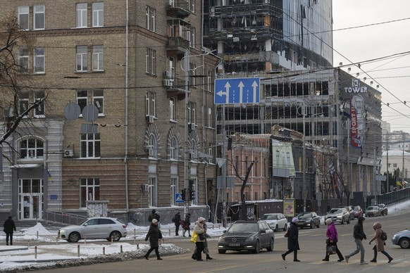11.01.2023, Ukraine, Kiew: Menschen überqueren eine Straße, an der Häuser stehen, die nach ukrainischen Angaben durch russischen Beschuss beschädigt wurden. Foto: Andrew Kravchenko/AP/dpa +++ dpa-Bild ...