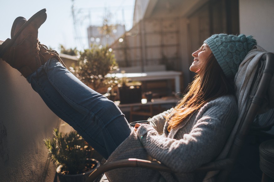 Photo of a young woman taking a few minutes off to relax on the balcony over the city, on a beautiful, sunny, autumn day