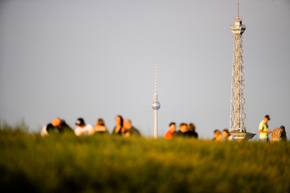 Menschen genießen vor dem Berliner Fernsehturm (M) und dem Funkturm den sonnigen Abend auf dem Drachenberg.