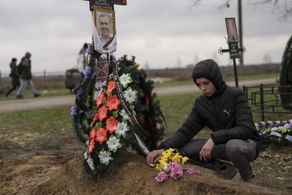 Der 15-jährige Jura Nechyporenko legt auf dem Friedhof in Butscha Schokolade auf das Grab seines Vaters Ruslan.