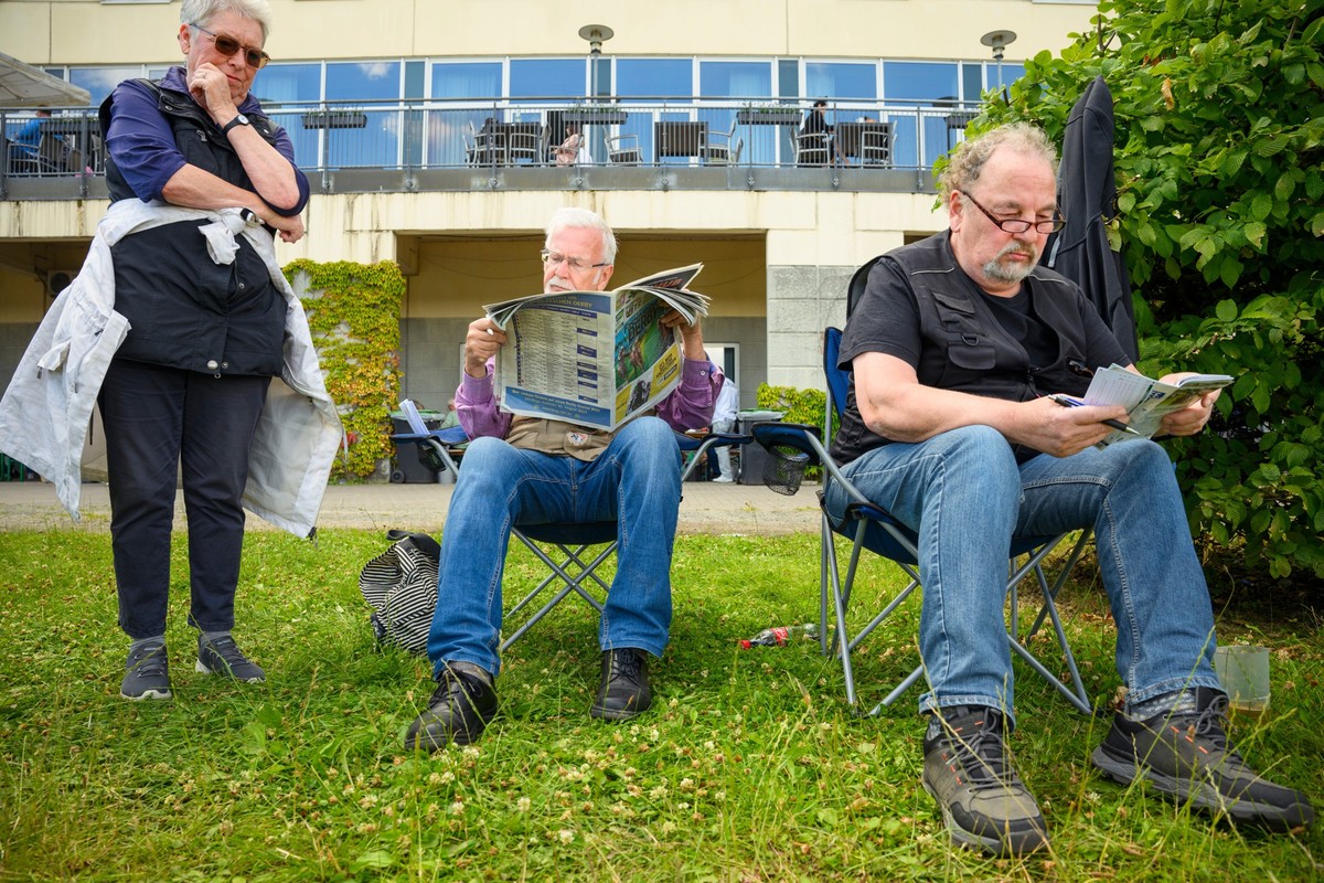 07.07.2024, Hamburg: Pferderennen: Idee Derby-Meeting 2024 auf der Galopprennbahn in Hamburg Horn. Zuschauende sitzen auf Campingstühlen am Rand der Laufbahn und lesen die Zeitung des Renntages. Foto: ...