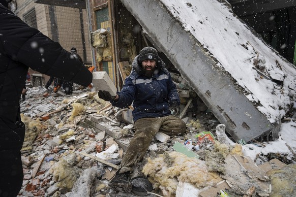 dpatopbilder - 03.01.2024, Ukraine, Kiew: Ein Freiwilliger räumt die Trümmer eines Wohnhauses weg, das gestern bei einem russischen Angriff schwer beschädigt wurde. Foto: Evgeniy Maloletka/AP/dpa +++  ...