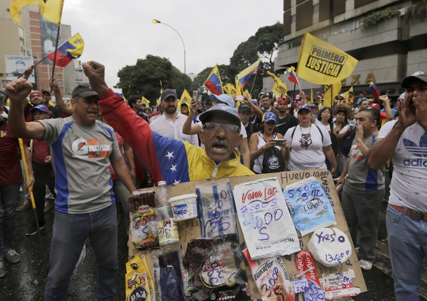 An opposition member holds a poster board with the prices of basic food during a protest against Venezuela's President Nicolas Maduro in Caracas, Venezuela, Wednesday, Jan. 23, 2019. Venezuela's re-in ...