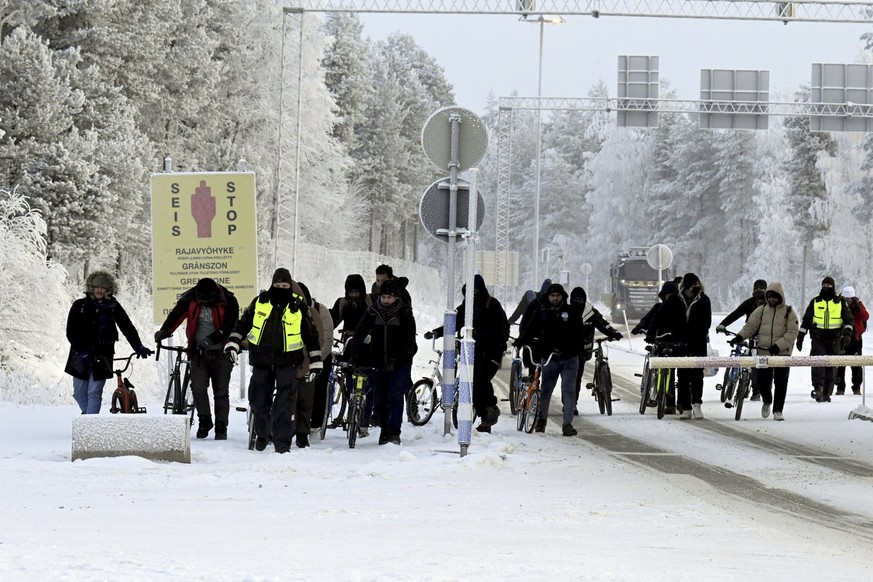 21.11.2023, Finnland, Salla: Finnische Grenzschutzbeamten eskortieren Migranten mit Fahrrädern am internationalen Grenzübergang in Salla. Seit Finnland vier Grenzstationen zu Russland geschlossen hat, ...