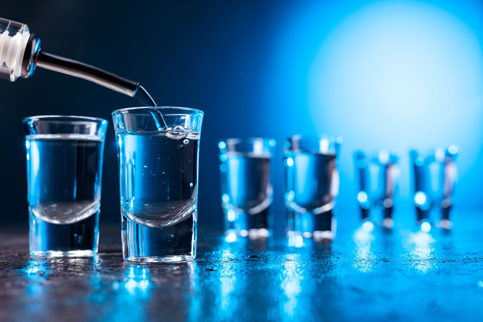 Vodka poured into a glass lit with blue backlight. Copy space.