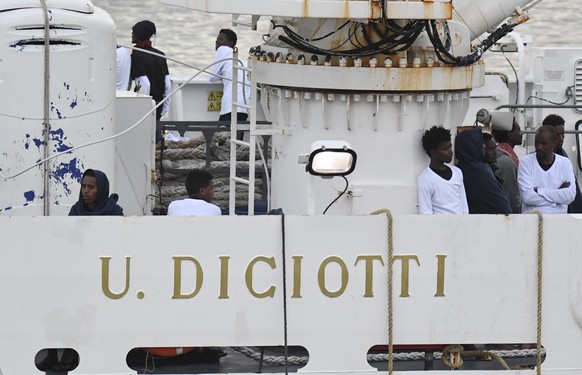 Migrants stand on the deck of the Italian Coast Guard ship Diciotti, moored at the Catania harbor, Tuesday, Aug. 21, 2018. One and seventy-seven migrants rescued at sea remained aboard the Italian Coa ...