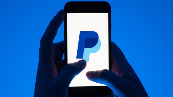 ARCHIV - 12.05.2022, Sachsen, Dresden: ILLUSTRATION - Eine Frau hält ein Smartphone mit dem Logo des Bezahldienst Paypal. (gestellte Szene) Paypal gibt am 03.11.2022 Zahlen für das 3. Quartal bekannt. ...