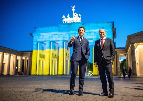 Bundeskanzler Olaf Scholz (r, SPD) und Frankreichs Präsident Emmanuel Macron stehen nach einem Treffen vor dem Brandenburger Tor. Aus Anlass des Europatages ist das Brandenburger Tor in den ukrainisch ...