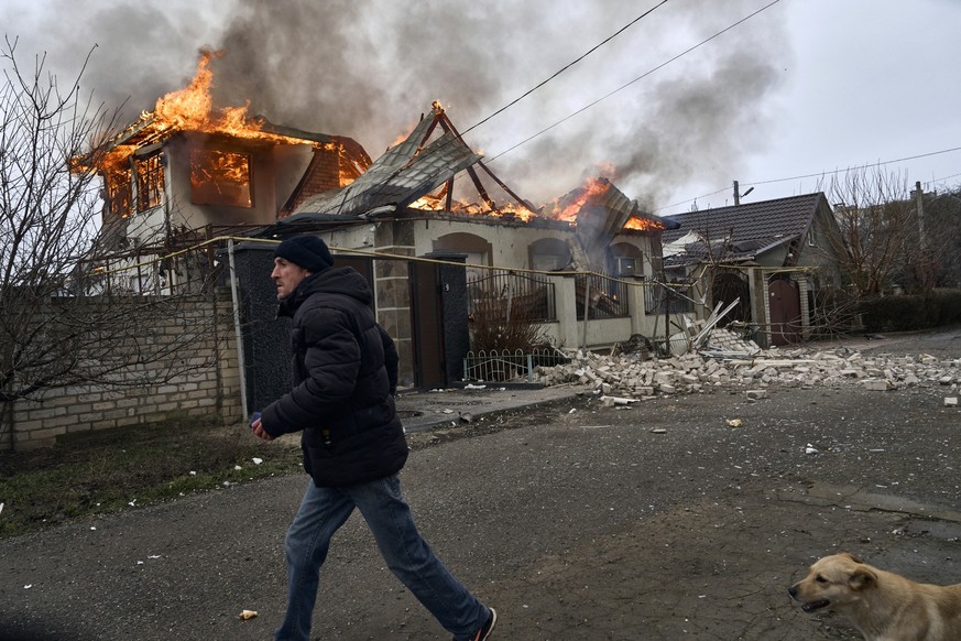 06.01.2023, Ukraine, Cherson: Ein Anwohner läuft an einem brennenden Haus vorbei, das nach ukrainischen Angaben bei russischem Beschuss am orthodoxen Weihnachtsabend getroffen wurde. Foto: Libkos/AP/d ...