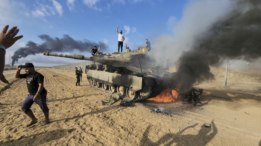 07.10.2023, Palästinensische Gebiete, Khan Younis: Palästinenser feiern an einem zerstörten israelischen Panzer am Zaun des Gazastreifens östlich von Khan Younis. Die islamistische Hamas hat vom Gazas ...