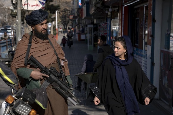 26.12.2022, Afghanistan, Kabul: Ein Taliban-Kämpfer steht Wache, während eine Frau vorbeiläuft. Jüngste Entscheidungen der Taliban über afghanische Frauen, darunter das Verbot der Universitätsausbildu ...