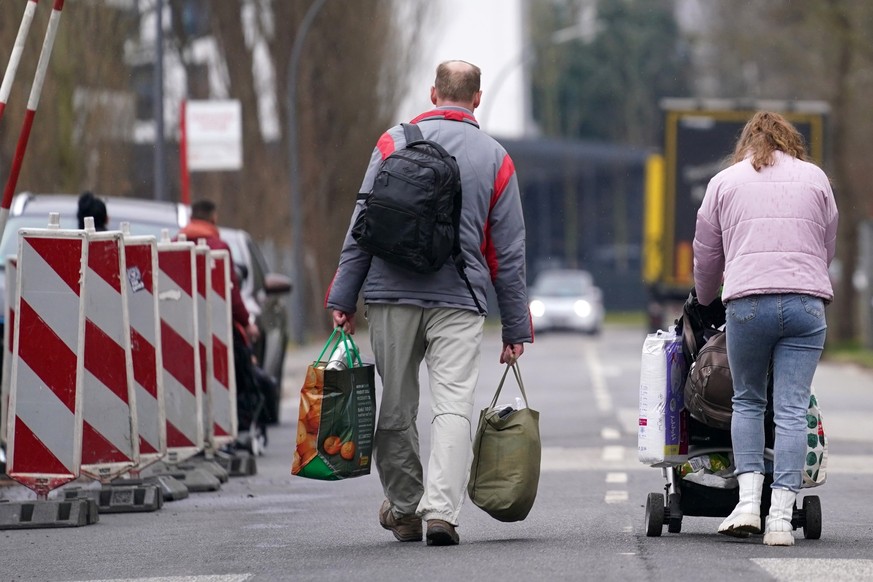 ARCHIV - 14.03.2022, Hamburg: Ein aus der Ukraine geflüchteter Mann und eine Frau mit Kinderwagen verlassen mit ihrem Gepäck die Flüchtlingsunterkunft im ehemaligen Fegro Großmarkt im Stadtteil Harbur ...