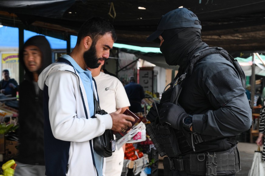 Russia Migrants 8742705 13.08.2024 A serviceman of the Russian National Guard Rosgvardiya checks the documents of migrants in Novosibirsk, Russia. Following an inspection of 400 citizens, more than 20 ...