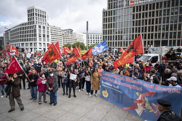 03.10.2022, Berlin: Teilnehmer stehen auf der Demonstration «Heizung, Brot &amp; Frieden! Protestieren statt frieren» am Potsdamer Platz mit Fahnen und Plakaten. Die Demo wird von einem Bündnis versch ...