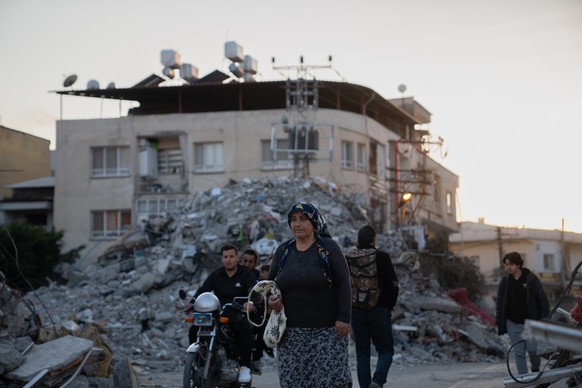 23.02.2023, Türkei, Iskenderun: Menschen gehen an den Trümmern von Gebäuden vorbei, die durch das Erdbeben eingestürzt sind. Zweieinhalb Wochen nach der Erdbeben-Katastrophe im türkisch-syrischen Gren ...