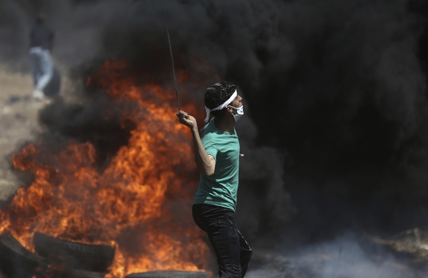 A Palestinian protester hurls stones at Israeli troops during a protest at the Gaza Strip's border with Israel, Monday, May 14, 2018. Thousands of Palestinians are protesting near Gaza's border with I ...