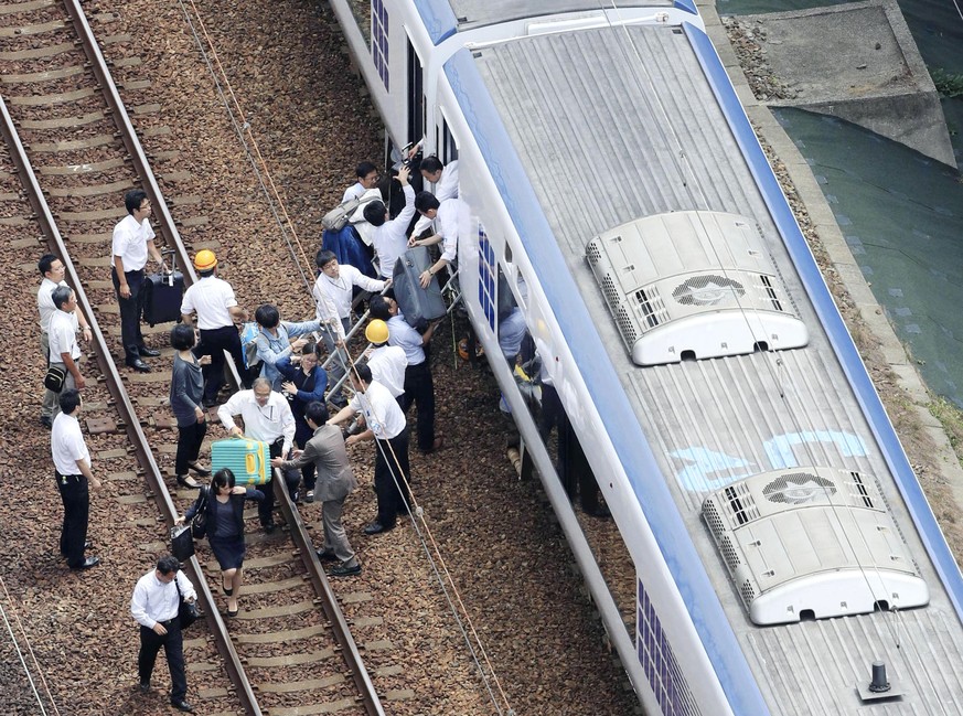 Passengers descend from a train on the track after train service was suspended to check for damage following an earthquake in Takatsuki city, Osaka, western Japan, Monday, June 18, 2018. A strong eart ...