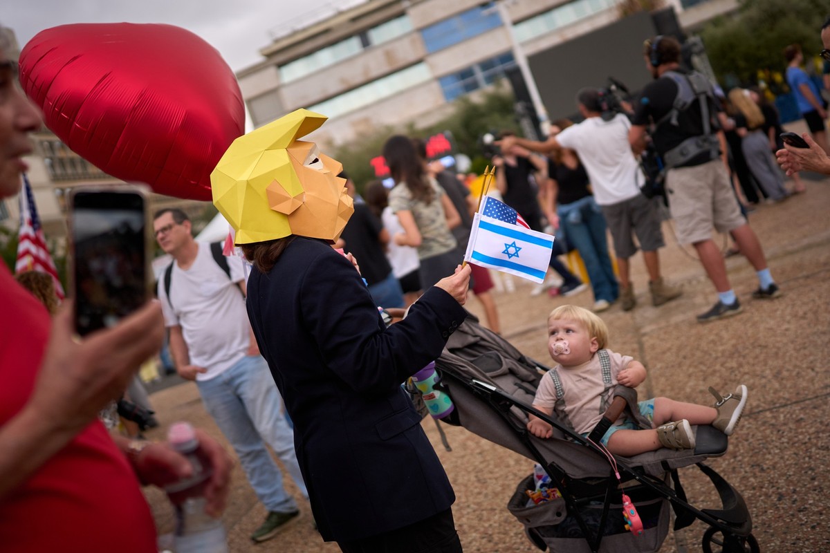 A child watches at a person wearing a mask depicting U.S. President Donald Trump as relatives and supporters of Israeli hostages held by Hamas in the Gaza Strip celebrate following the announcement th ...