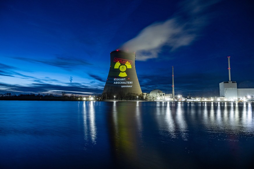 09.03.2023, Bayern, Niederaichbach: Greenpeace-Aktivisten projizieren eine abgelaufene HU-Plakette auf den K