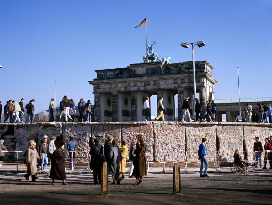 Mauerspaziergang - Menschen stehen auf der Berliner Mauer kurz nach der Wende