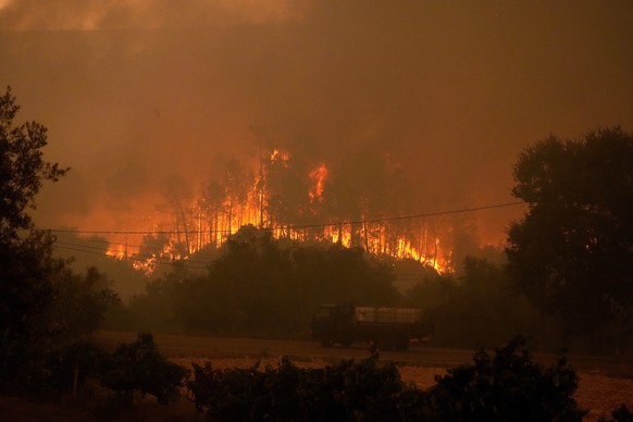 13.07.2022, Portugal, Ansiao: Ein Lastwagen mit Wassertanks f�hrt an einem Waldbrand vorbei, w�hrend Rauch den Himmel im Dorf Bemposta in der N�he von Ansiao verdunkelt. Tausende von Feuerwehrleuten k ...