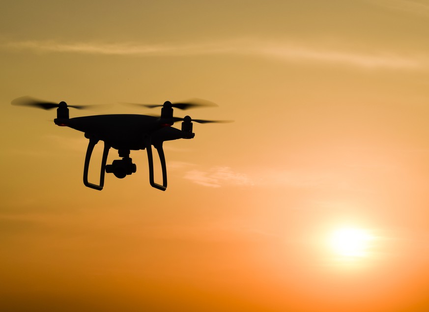 Quadrocopters silhouette against the background of the sunset. Flying drones in the evening sky.