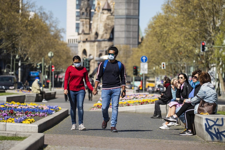 Menschen spazieren mit Mundschutzmasken in Berlin am 22. April 2020. Ab heute koennen in Berlin laeden unter 800 qm, Buchhandlucngen und Autosalons wieder oeffnen mit Einhanltung von Hygiene und Dista ...