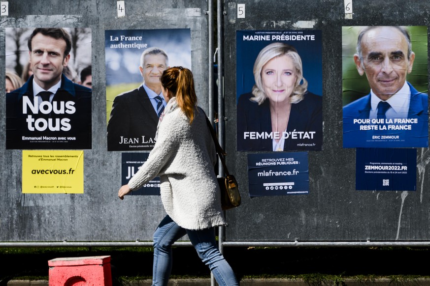 Deux personnes marchent devant les affiches des candidats Emmanuel Macron, Jean Lassalle, Marine Le Pen et Eric Zemmour, pour la prochaine election presidentielle francaise le mercredi 6 avril 2022 a  ...