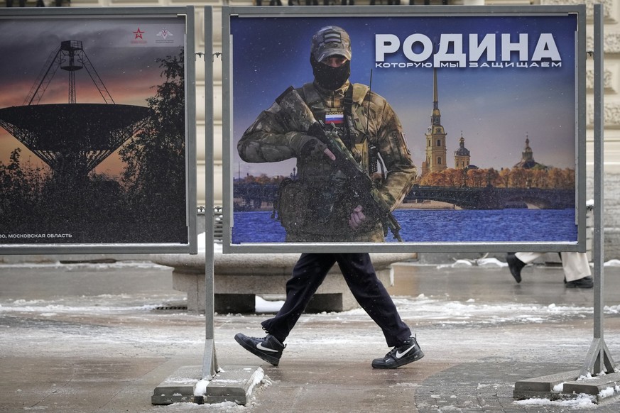ARCHIV - 20.02.2023, Russland, St. Petersburg: Ein Mann geht an einem Plakat mit dem Bild eines russischen Soldaten und der Aufschrift «Wir verteidigen das Vaterland» vorbei, während einer Straßenauss ...